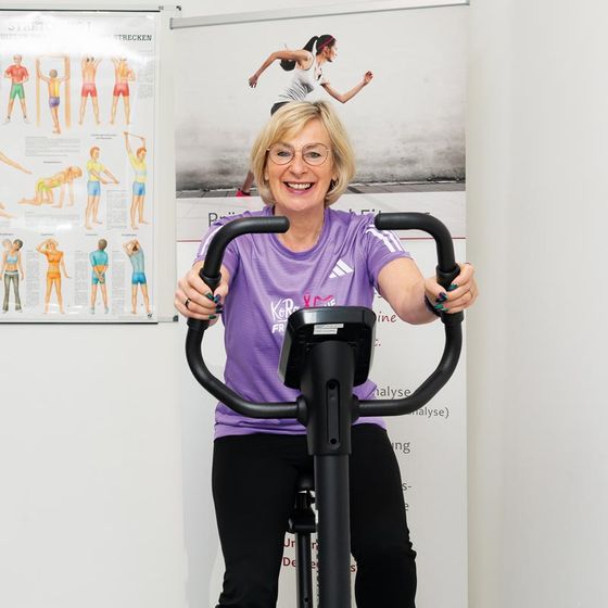 Eine Frau trainiert strahlend auf dem Ergometer